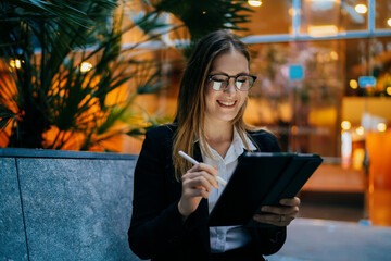 Smiling businesswoman with stylus and tablet, sitting comfortably while working, highlighting joy, control, and flexibility in digital freelance lifestyle