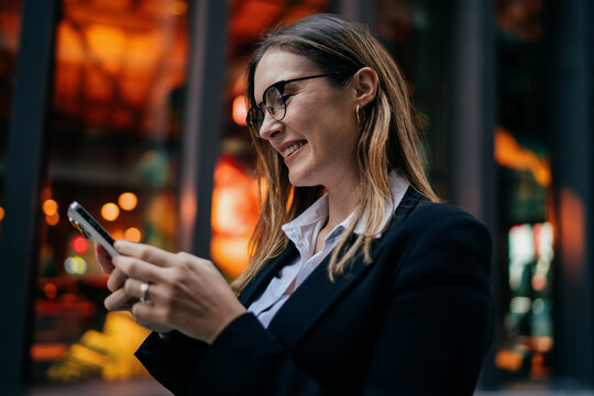 Young woman laughing while using smartphone in urban space, expressing digital ease, confidence, and flexible communication in freelance lifestyle