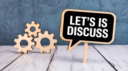 A small chalkboard sign shaped like a speech bubble with the words lets is discuss written in white chalk next to wooden gears on a rustic wooden surface with a textured blue background