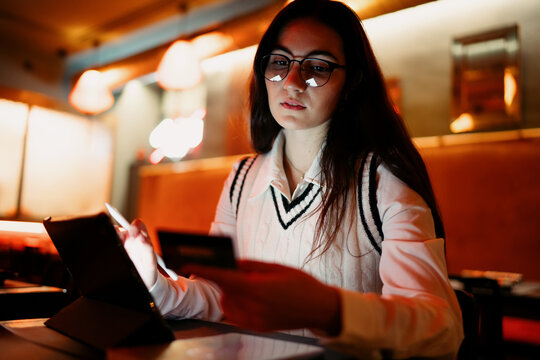 Woman interacting with a tablet and holding a card in ambient light, representing modern finance behavior, digital shopping, and seamless user experience in a connected ecosystem.