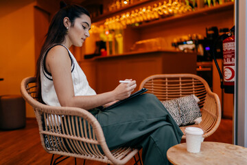 Concentrated woman works with stylus and tablet in cozy public lounge, showing casual digital productivity and hands-on interaction with modern technology.