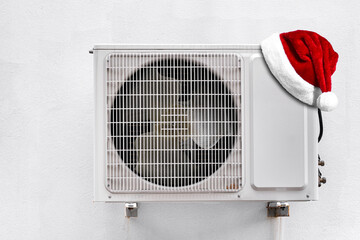 Santa Claus Hat on air conditioner system on wall. Fan box outdoors. Christmas and New Year celebration
