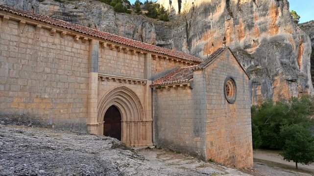 The hermitage of Saint Bartolome rises against canyon cliffs in the canyon of Rio Lobos in Soria. its stone walls and Gothic arch revealed in a smooth panoramic shot of this historic Templar sanctuary