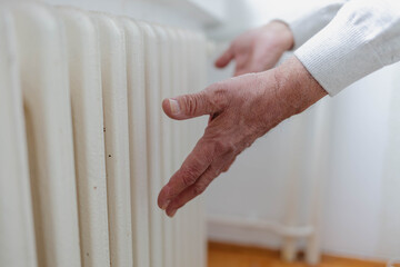 Senior man is getting his hands warm on central heating system.