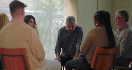Man speaks during group therapy session, leaning forward while engaging with others in supportive...