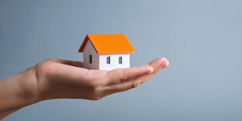 Hand holding miniature house with orange roof against gray background