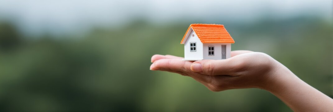 Female hand holding miniature house against blurred green background - Powered by Adobe