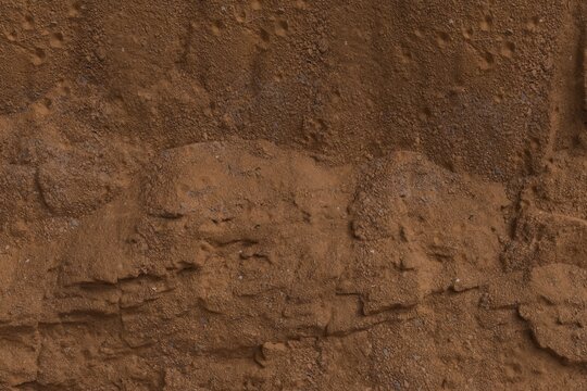 Close-up of a textured, layered reddish-brown earth/rock formation. Visible strata show varying granularity and eroded patterns, suggesting a natural geological cross-section