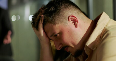 Man clutching head in distress after confrontation in modern office, experiencing emotional...