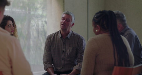 Man speaks emotionally during group therapy session, surrounded by peers in quiet circle as he...