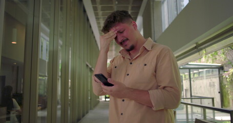 Man covering face in emotional distress while reading phone, overwhelmed by bad news or personal...