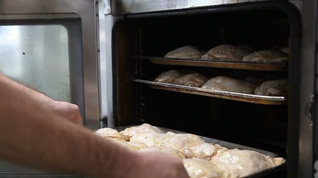 The cook inserts a baking tray with chicken legs into the combi steamer.