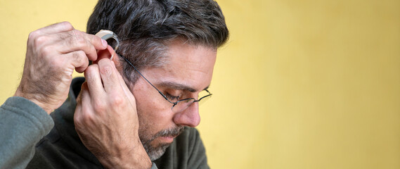 Man putting a modern hearing aid in his ear for better hearing