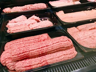 Ground Meat Patties and Sausages in Refrigerator Case. Black trays filled with fresh minced meat patties and raw sausages ready for sale in supermarket refrigerated section. BBQ and cooking concept.