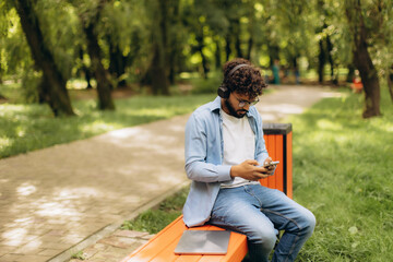 Young man using phone, listening to music in park