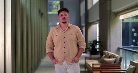 Fototapeta premium Man standing in office hallway with clenched fists and determined expression, posed in modern corridor with seating area in background