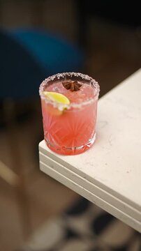 A glass of pink drink with a lime slice in it. The drink is on a table. The table is white and has a black border