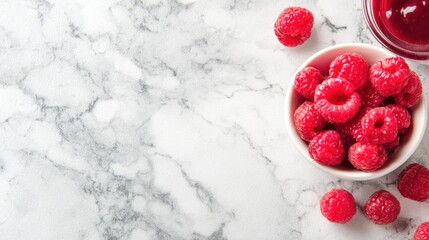 Fresh raspberries in a bowl beside a glass of raspberry juice on marble surface
