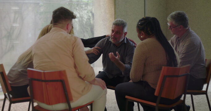 Man opens up emotionally during group therapy session, leaning forward while expressing vulnerability and receiving support from compassionate peers seated in circle