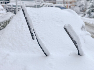 Snow covered car with raised windshield wipers in heavy winter snowfall