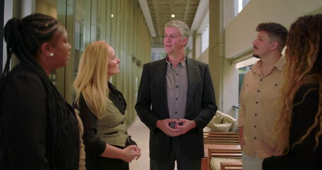 Manager addressing team in office hallway, group of diverse professionals listening during...