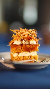 A slice of carrot cake with a spoon on a plate. The cake is topped with carrot pieces and has a light, fluffy texture