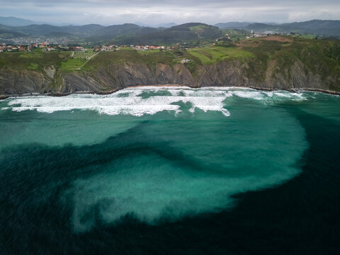Example of the rip current in the ocean. Aerial view of turquoise sea full of sediment and the dramatic coastline of northern Spain.
