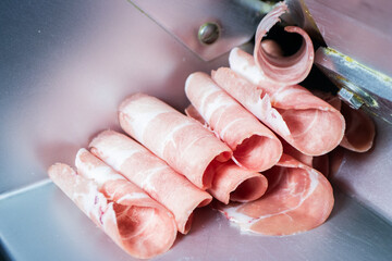 Thinly sliced raw pink meat (pork or beef) rolled up, freshly cut by a meat slicer machine, ready for hot pot or shabu-shabu.