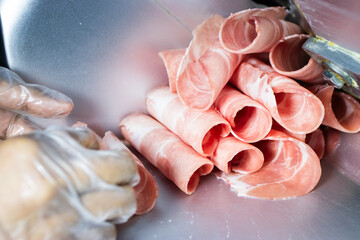 Thinly sliced raw pink meat (pork or beef) rolled up, freshly cut by a meat slicer machine, ready for hot pot or shabu-shabu.