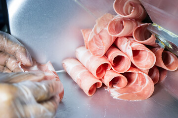 Thinly sliced raw pink meat (pork or beef) rolled up, freshly cut by a meat slicer machine, ready for hot pot or shabu-shabu.