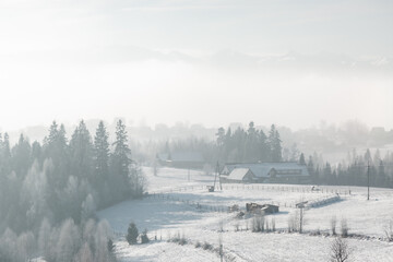 Snowy winter Buflak village shrouded in morning mist over frosty fields and forest