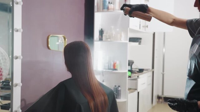 hair treatment application, professional stylist spritzes lengthy hair, beauty specialist administers mist on long strands, customer receives treatment spray from stylist in salon environment