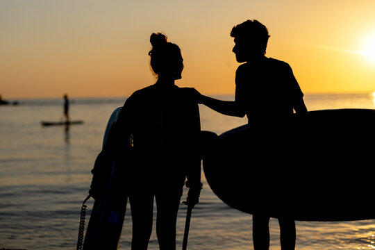 Beautiful young surfer couple walking on the beach during sunset and looking at the ocean. Sport