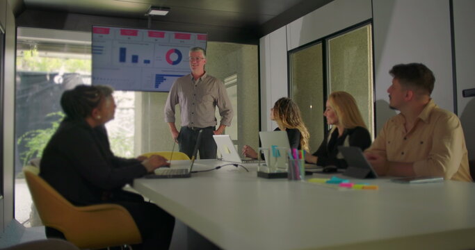 Manager presenting data on screen while diverse team of professionals watch presentation in modern conference room with natural light - Powered by Adobe