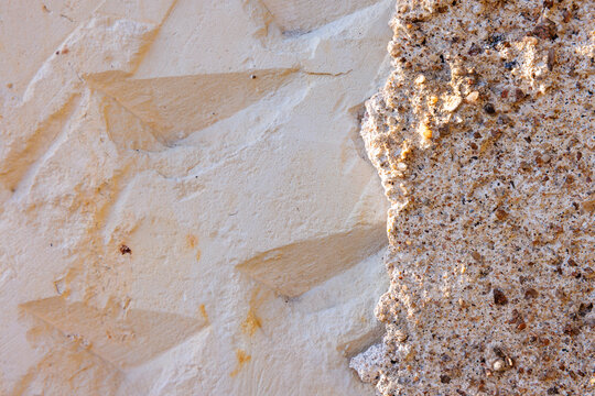Textured stucco wall with carved shapes meets exposed aggregate concrete, contrasting smooth and rough materials, architectural background highlighting surface detail and craft.