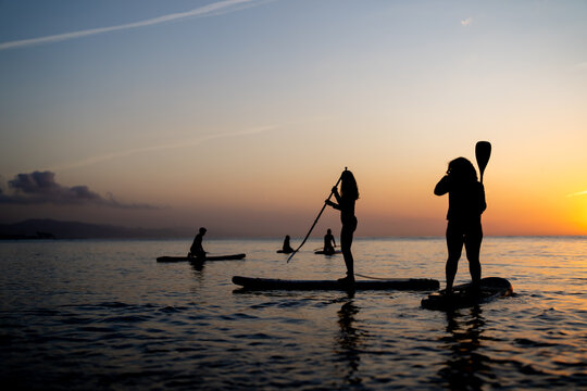 People paddle boarding together on calm water at sunset create a peaceful lifestyle outdoor