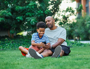 Portrait of father and son having fun using a mobile phone outdoors in park or nature,, family...