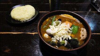a bowl of hearty soup curry with colorful vegetables. Sapporo Soup Curry is a cozy Japanese dish of tender chicken and crispy fried vegetables in a light broth with curry powder and garam masala