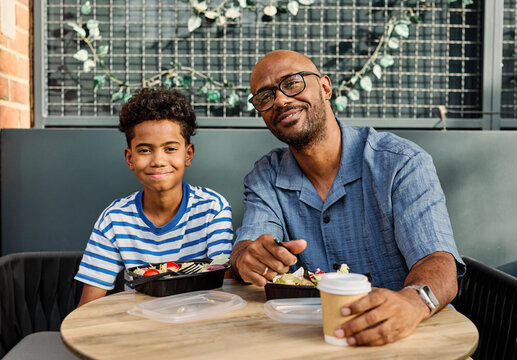 Portrait of father and son having fun outdoors in park sitting and eating during a break, family life, parenting, love and bonding concepts - Powered by Adobe