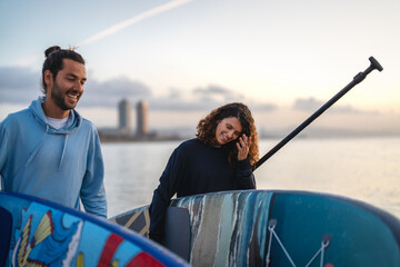 Friends share a joyful moment at the beach during sunset, holding vibrant surfboards while laughing