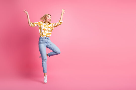 Young woman jumps with joy in pink studio wearing yellow tie dye shirt and jeans for a vibrant lifestyle fashion ad