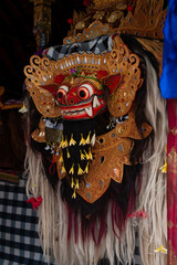 Close up of traditional Balinese Barong mask. Mythological lion creature symbol of good spirit in Hindu culture. Sacred wooden carving with gold ornaments and flowers in Bali, Indonesia.
