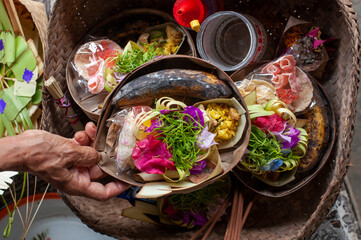 Top view of traditional Balinese Hindu offering Canang sari in woven basket. Hand holding daily prayer ritual sacrifice with flowers and rice in Bali Indonesia.