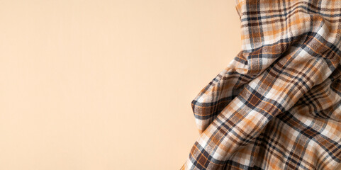 Wrinkled in folds plaid brown orange flannel cotton fabric on beige plain background, top view....