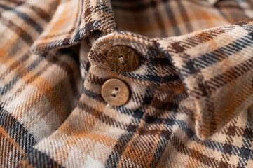 Obraz premium Close-up of plaid shirt detail. Brown and orange cotton flannel shirt, details of the collar, sleeves, pockets, coconut buttons. Clothing texture, tartan pattern. Autumn winter casual shirt