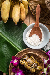 A beautifully arranged set of traditional Thai sticky rice desserts wrapped in banana leaves and tied with natural fibers, presented in a rustic bamboo basket. The scene features warm, cultural tones 