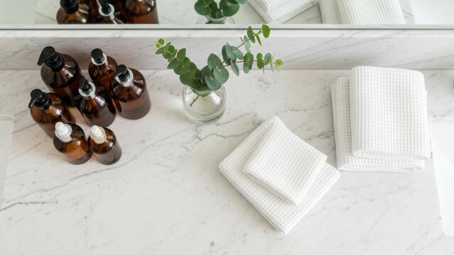 Amber glass bottles with pumps and folded white waffle towels on a marble countertop, bathroom vanity essentials, spa and wellness decor, clean and organized aesthetic