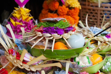Close up of Balinese Hindu offering Banten with egg, flowers and fruits. Sacred ritual sacrifice for ceremony. Traditional woven palm leaf basket on altar in Bali Indonesia.