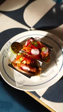 A plate of food with two tacos on it. The plate is on a table with a blue and white tile pattern