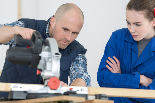 carpenter training female apprentice to use mechanized saw